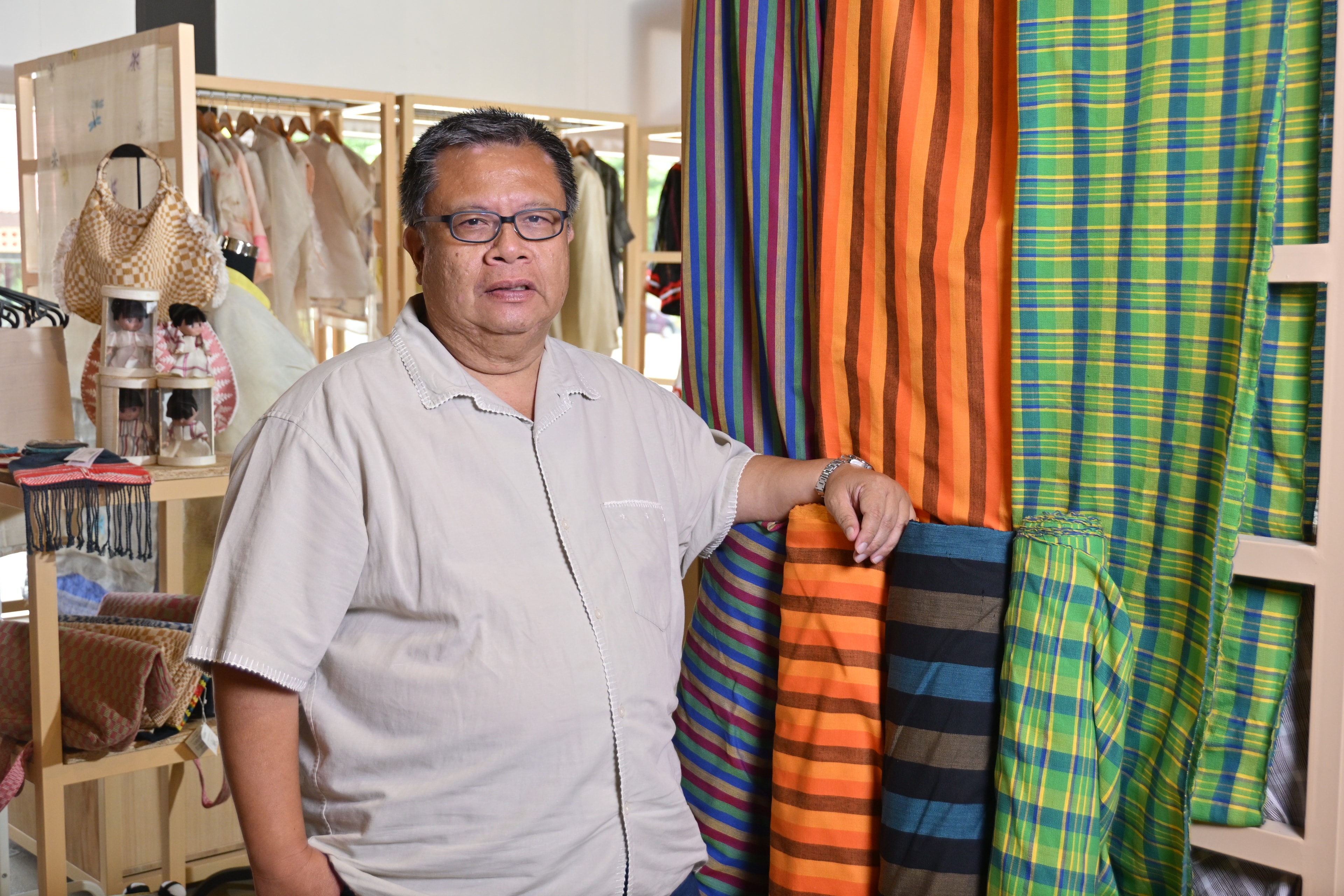 Al Valenciano standing with rolls of woven textiles